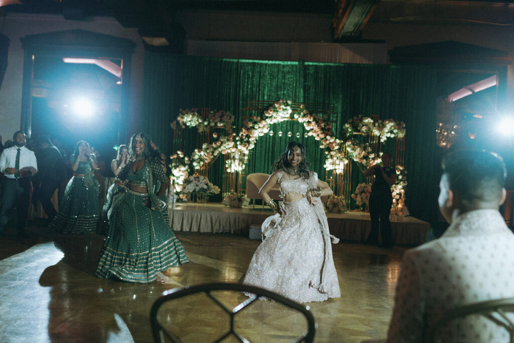 Bride performing a choreographed dance for the groom on a dazzling stage decorated with flowers at Crest Hollow Country Club, a stunning Indian catholic wedding venue on Long Island, captured by Elsie Goodman Photography.