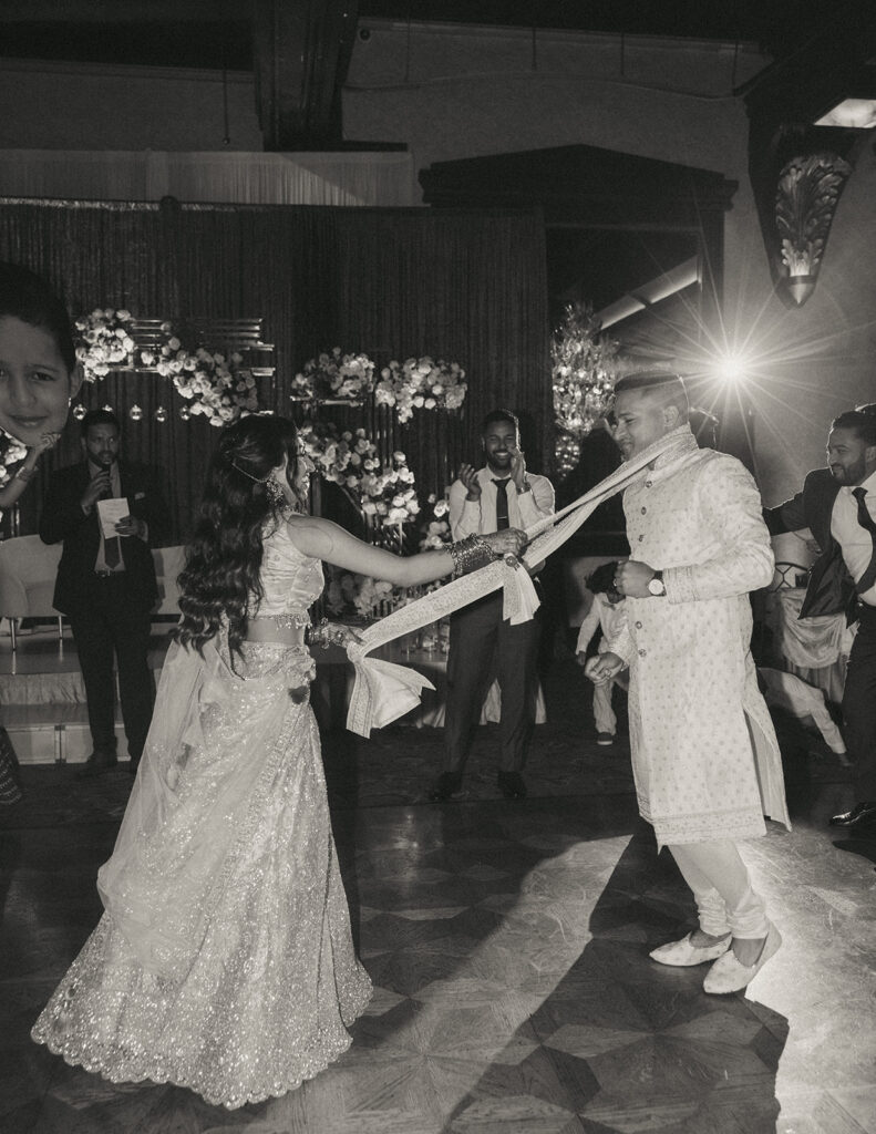 Bride playfully pulling the groom’s scarf on the dance floor during their Indian Catholic wedding reception at Crest Hollow Country Club, captured by Elsie Goodman Photography.