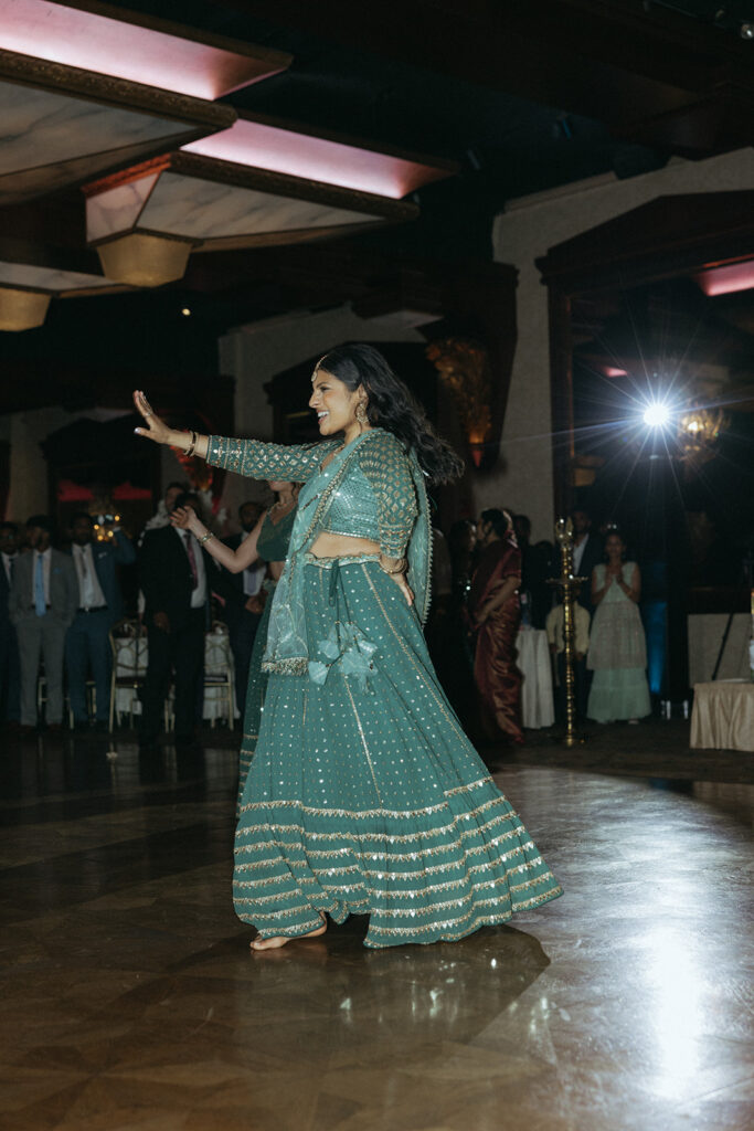 A woman in an emerald green lehenga dances barefoot at a lively Indian Catholic wedding reception at Crest Hollow Country Club, captured by Elsie Goodman Photography.