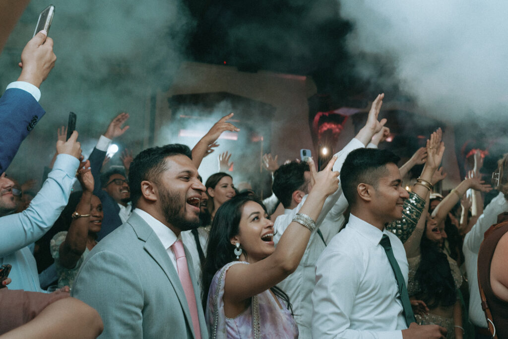 Wedding guests cheering with phones raised high during an epic celebration at a Catholic Indian wedding hosted at Crest Hollow Country Club, one of the best Indian wedding venues on Long Island, beautifully photographed by Elsie Goodman Photography.