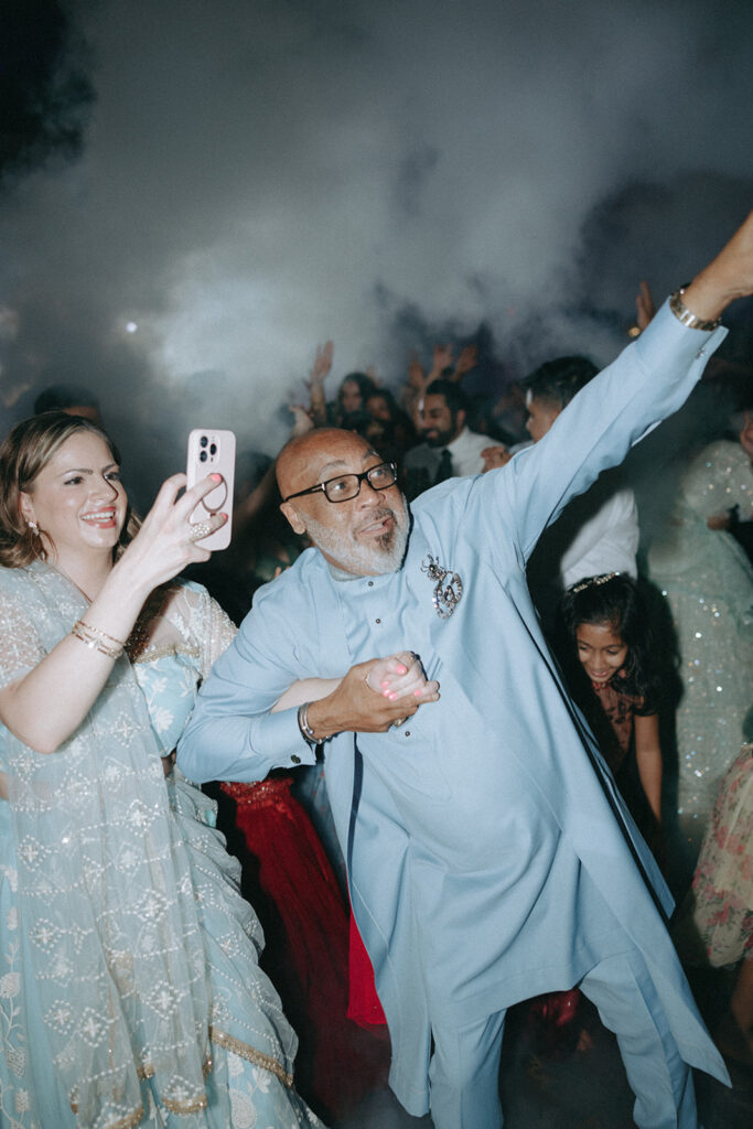 Guests dancing and celebrating through thick smoke effects at an unforgettable Catholic Indian wedding reception at Crest Hollow Country Club, one of the premier Indian wedding venues on Long Island, photographed by Elsie Goodman Photography.