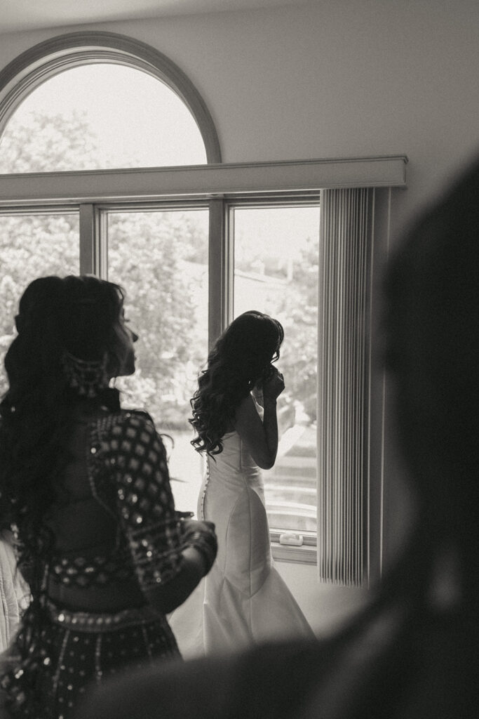 Bride standing by window putting on earrings before Catholic Indian wedding ceremony — Elsie Goodman Photography.