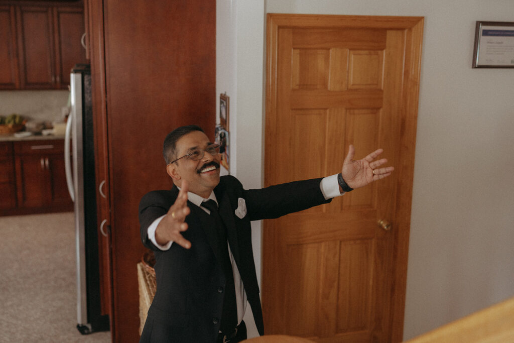Father smiling with arms outstretched during emotional first look with dad before Catholic Indian wedding — Elsie Goodman Photography.