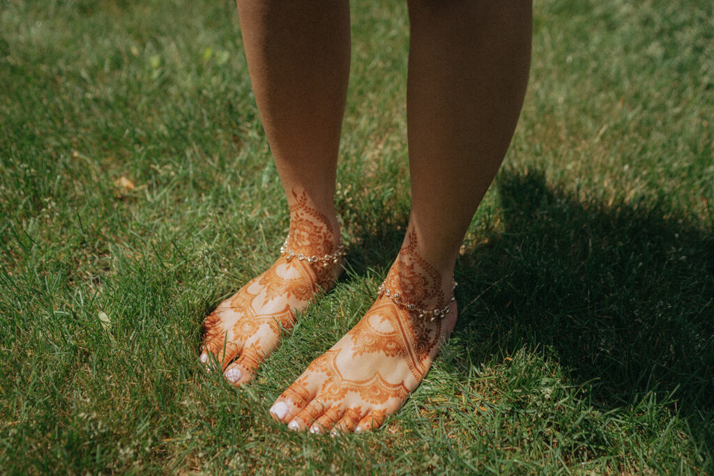 Bride’s mehndi-covered feet with anklets on grass before Catholic Indian wedding ceremony — Elsie Goodman Photography.