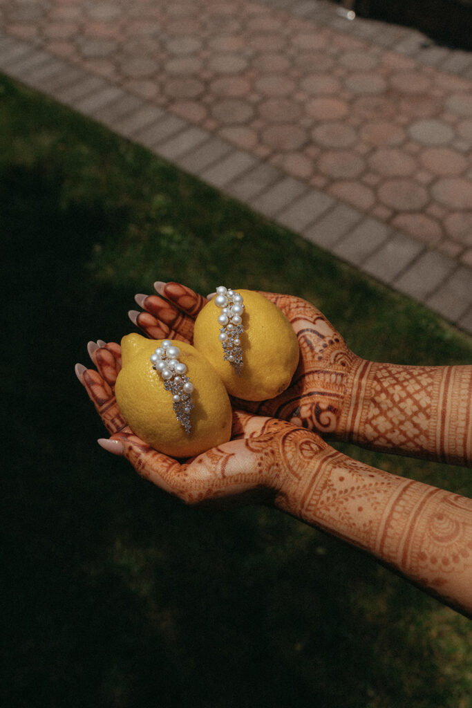 Bride’s mehndi-covered hands holding two lemons decorated with pearl jewelry for a traditional Catholic Indian wedding ritual, photographed by Elsie Goodman Photography.