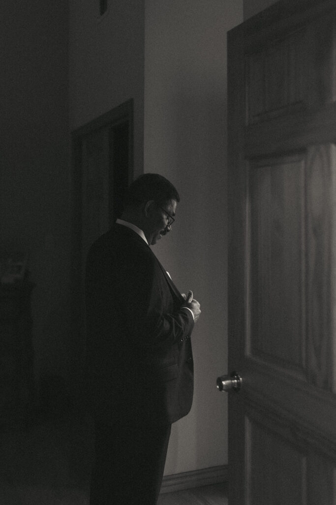 Father of the bride adjusting his suit jacket in a quiet, emotional moment before first look with dad at Catholic Indian wedding ceremony, captured by Elsie Goodman Photography.