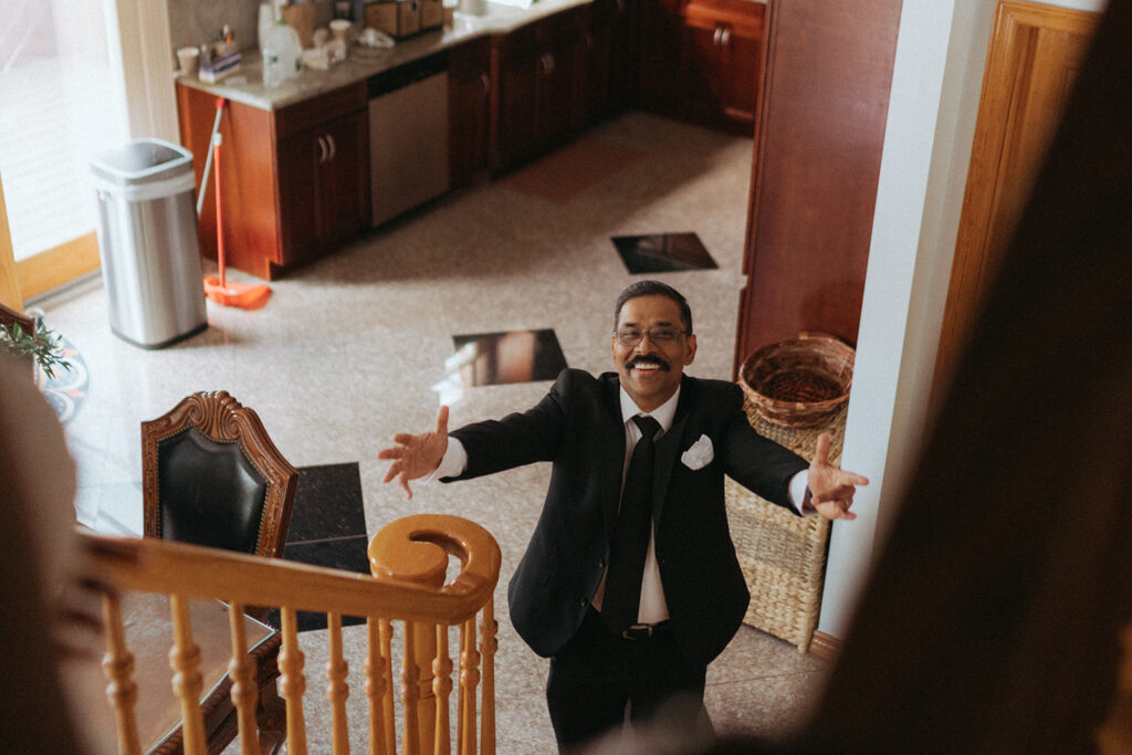 Father of the bride with open arms and joyful expression during first look with dad at Catholic Indian wedding, captured by Elsie Goodman Photography.