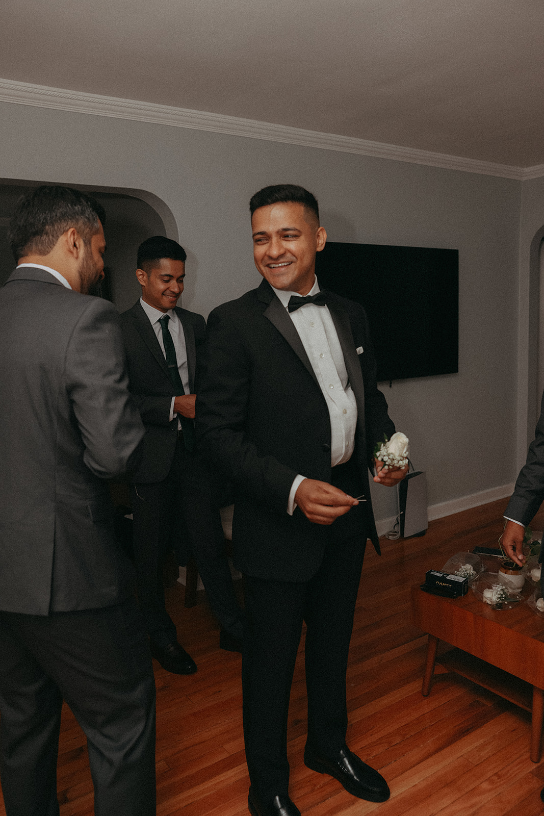 Groom laughing with groomsmen while preparing boutonnieres inside before Catholic Indian wedding ceremony, captured by Elsie Goodman Photography.