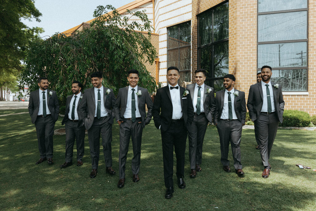Groom walking with his groomsmen outside the church, all wearing matching gray suits and green ties for a Catholic Indian wedding, photographed by Elsie Goodman Photography.
