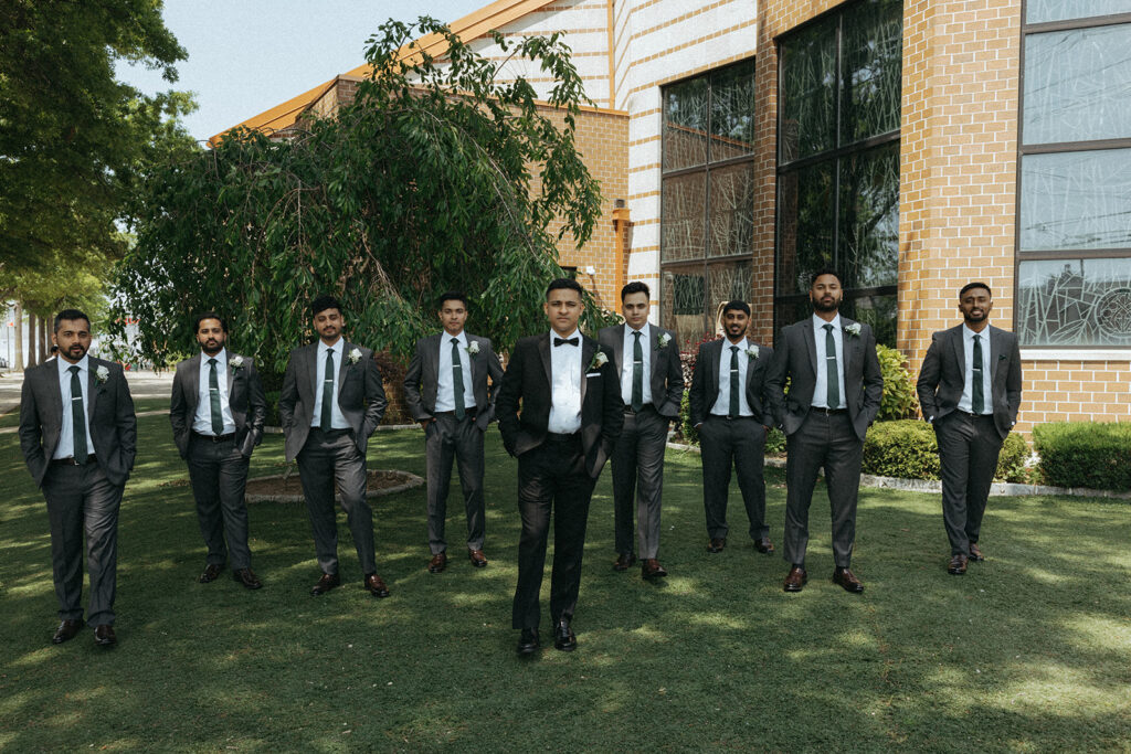 Groom standing confidently with his groomsmen lined up outside the church in matching gray suits, captured during Catholic Indian wedding portraits by Elsie Goodman Photography.
