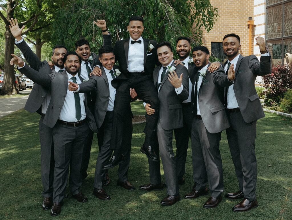 Groomsmen lifting the groom in celebration outside the church during Catholic Indian wedding festivities, captured by Elsie Goodman Photography.