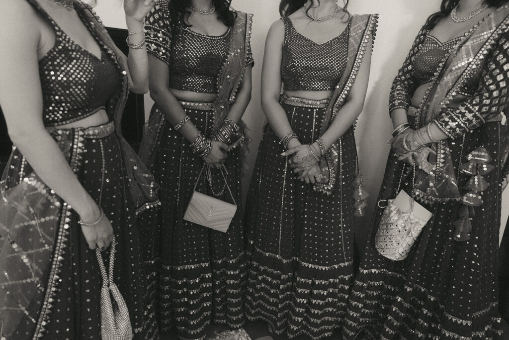 Bridesmaids in matching sparkling lehengas holding designer handbags, captured candidly before Catholic Indian wedding festivities, photographed by Elsie Goodman Photography.