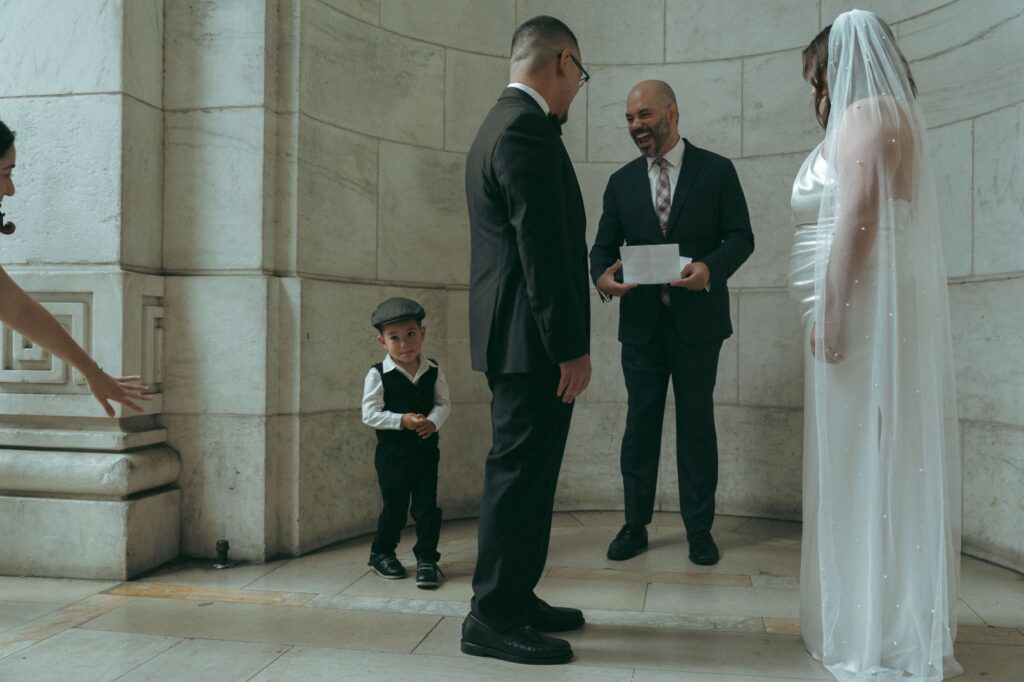 Little boy runs around altar during NYPL wedding ceremony while officiant laughs, shot by Elsie Goodman.