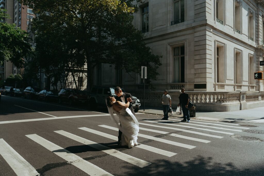Groom dips bride in crosswalk outside New York Public Library after elopement, NYPL wedding by Elsie Goodman.
