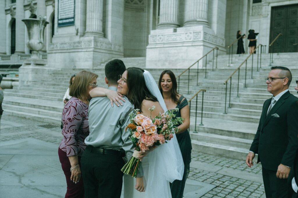 Bride holds bouquet and hugs guest after NYPL wedding ceremony, shot by Elsie Goodman.