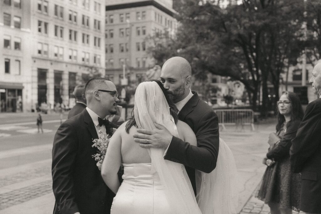Black and white photo of bride hugging a guest after New York Public Library wedding ceremony, by Elsie Goodman.