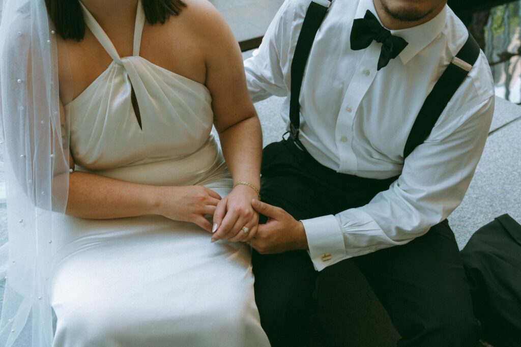 Close up of bride and groom sitting on a bench holding hands after eloping, shot by Elsie Goodman.
