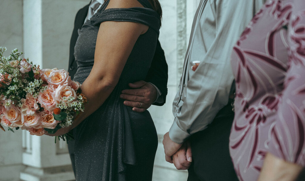 Close up of wedding guests with arms around each other holding the bride's bouquet at NYPL elopement, by Elsie Goodman.
