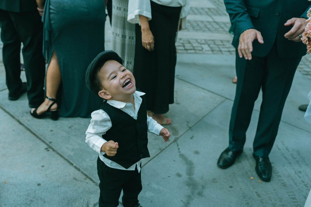 Little boy in wedding guest clothes laughing outside of New York Public Library, shot by Elsie Goodman.