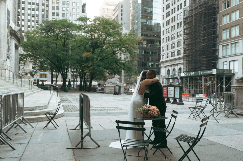 Father and daughter embrace outside the New York Public Library before her elopement, bouquet on table nearby, by Elsie Goodman.