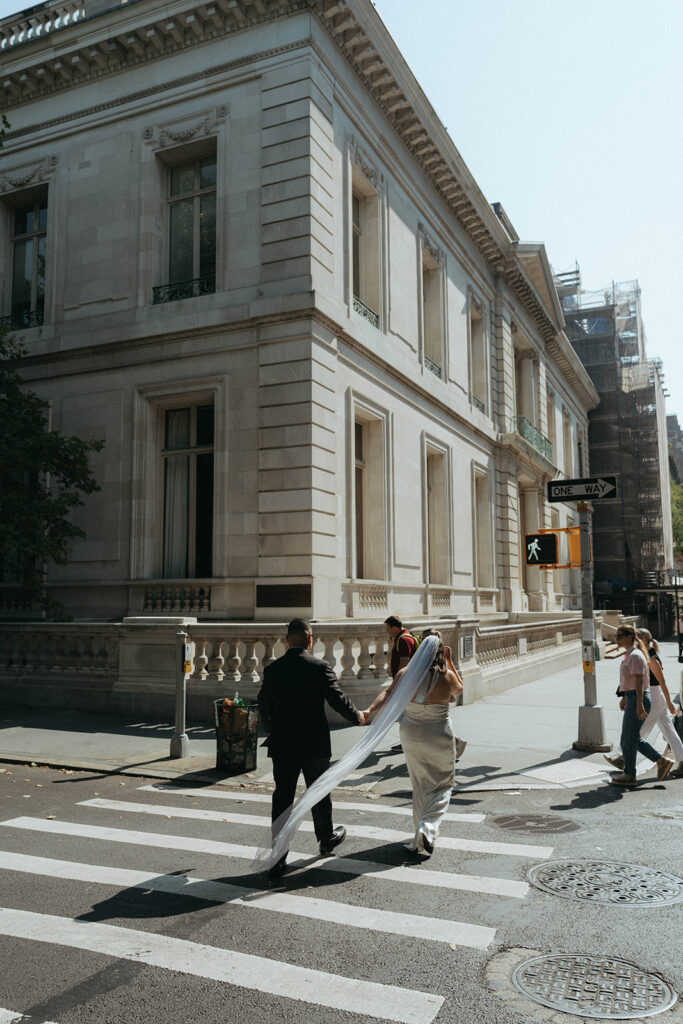 Bride and groom cross a NYC street after elopement, with the veil trailing behind her, captured by Elsie Goodman.