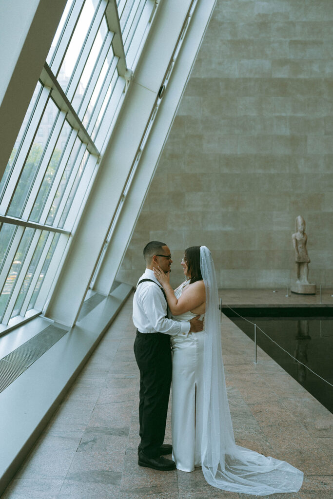 Bride and groom standing next to window and looking at each other for NYC wedding portraits, by Elsie Goodman.