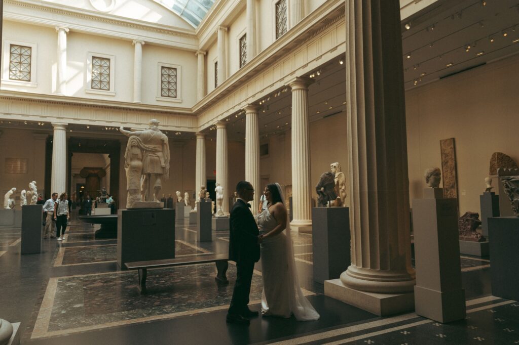 Couple stands holding hands inside the MET museum after their New York Public Library elopement, by Elsie Goodman.