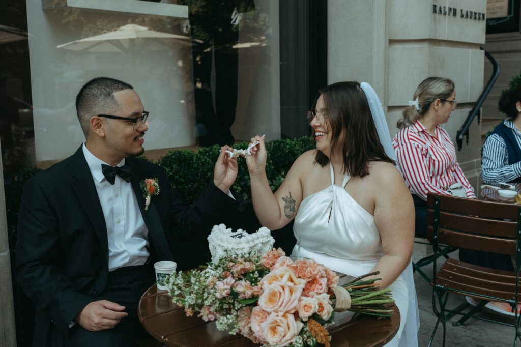 Couple feeds each other wedding cake outside Ralph Lauren café after their NYPL elopement, by Elsie Goodman.