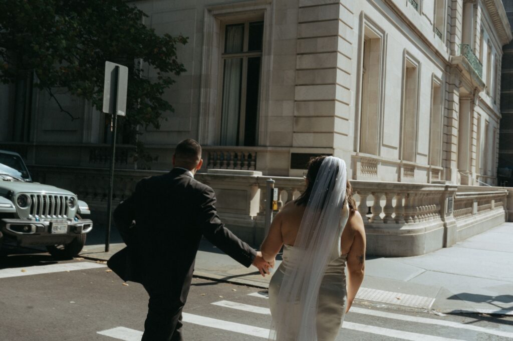 Groom leads bride across the street after New York Public Library wedding, photographed by Elsie Goodman.