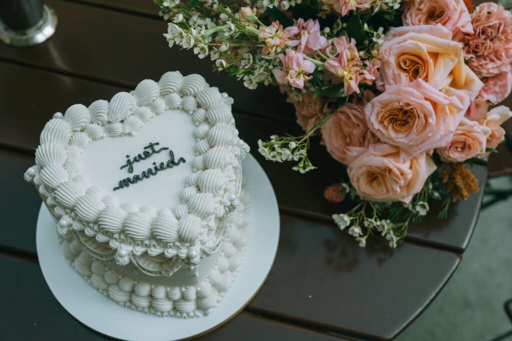 Heart-shaped “just married” cake beside rose bouquet at NYPL elopement, captured by Elsie Goodman.