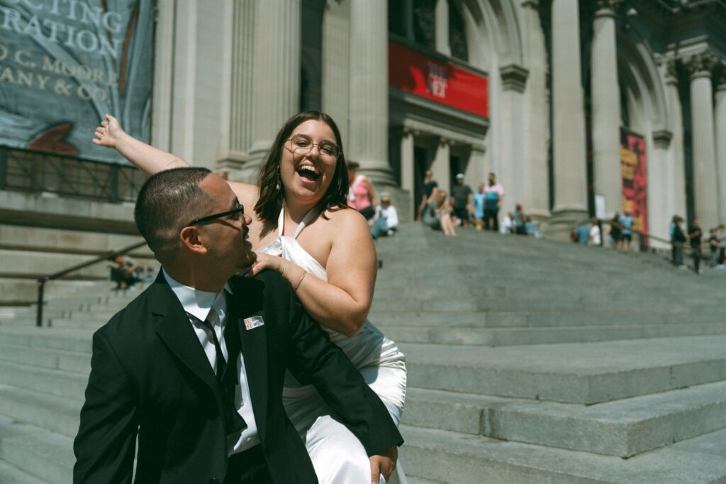 Bride laughs on groom’s back on MET steps after NYC elopement photo by Elsie Goodman.