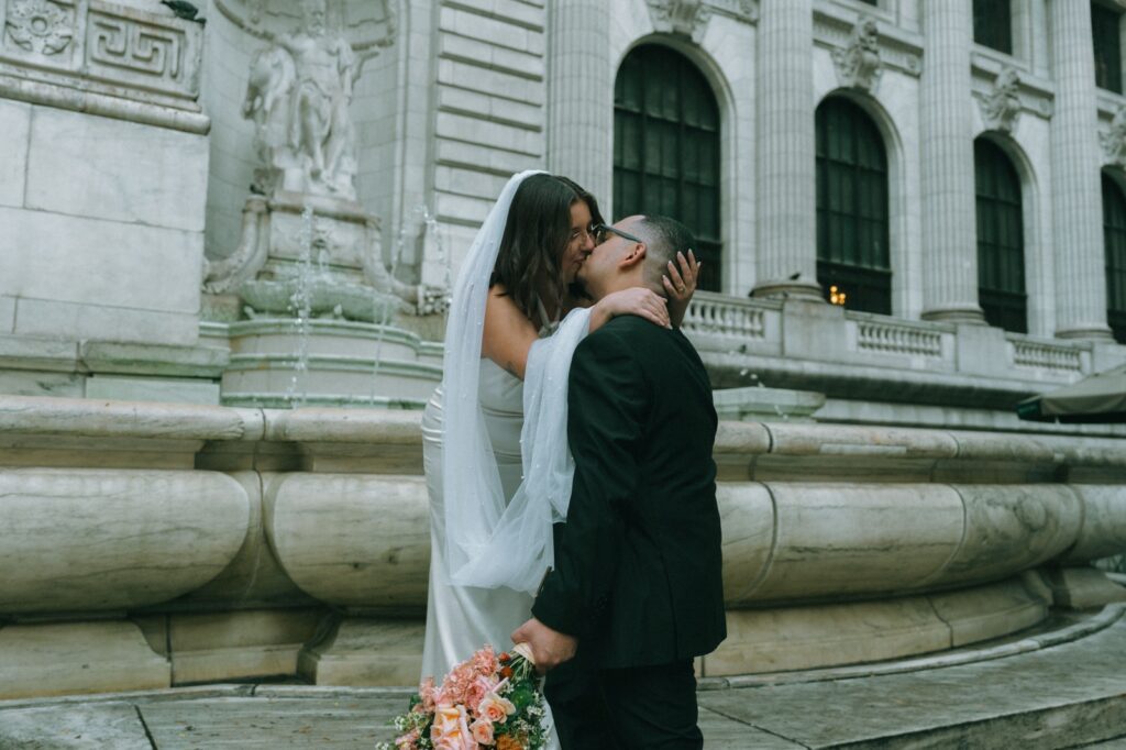 Bride and groom share kiss by NYPL fountain after elopement, photographed by Elsie Goodman.