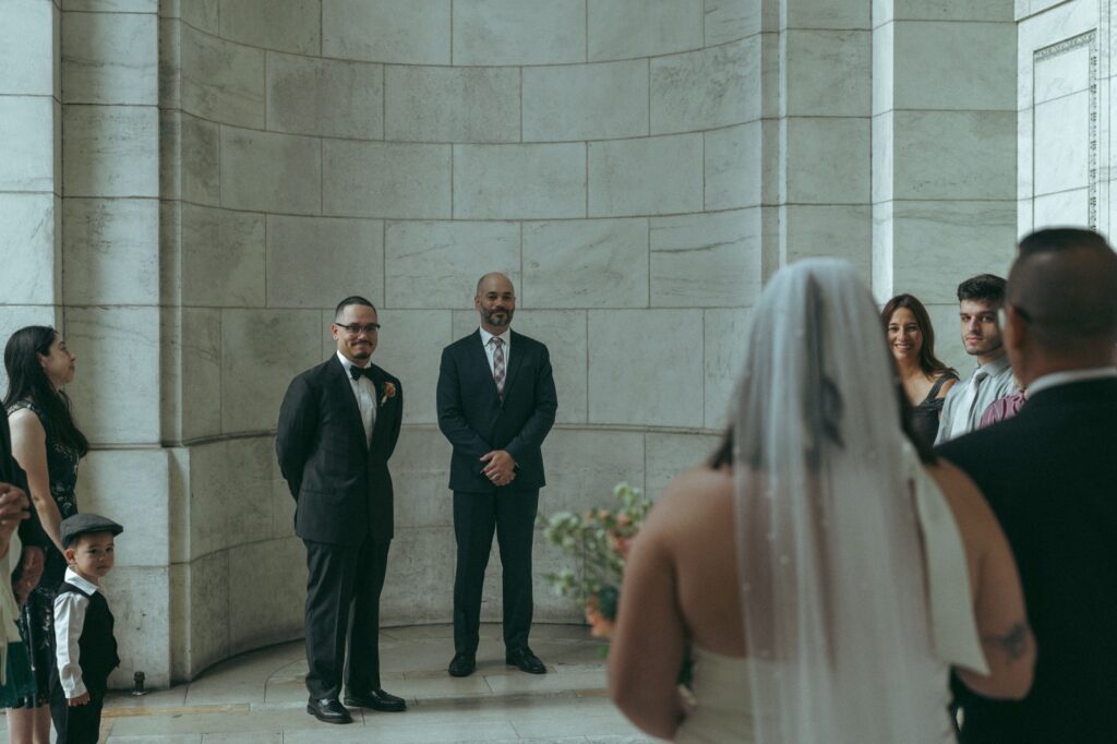 Groom and officiant face bride during New York Public Library wedding ceremony, photo by Elsie Goodman.