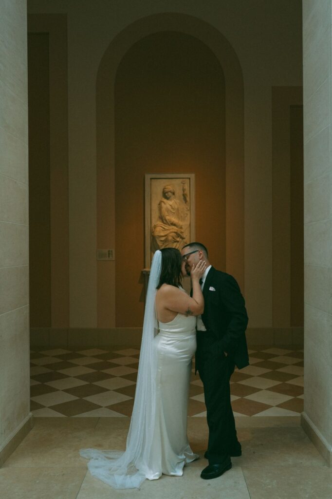 Bride and groom kiss under sculpture after NYPL elopement, photo by Elsie Goodman.