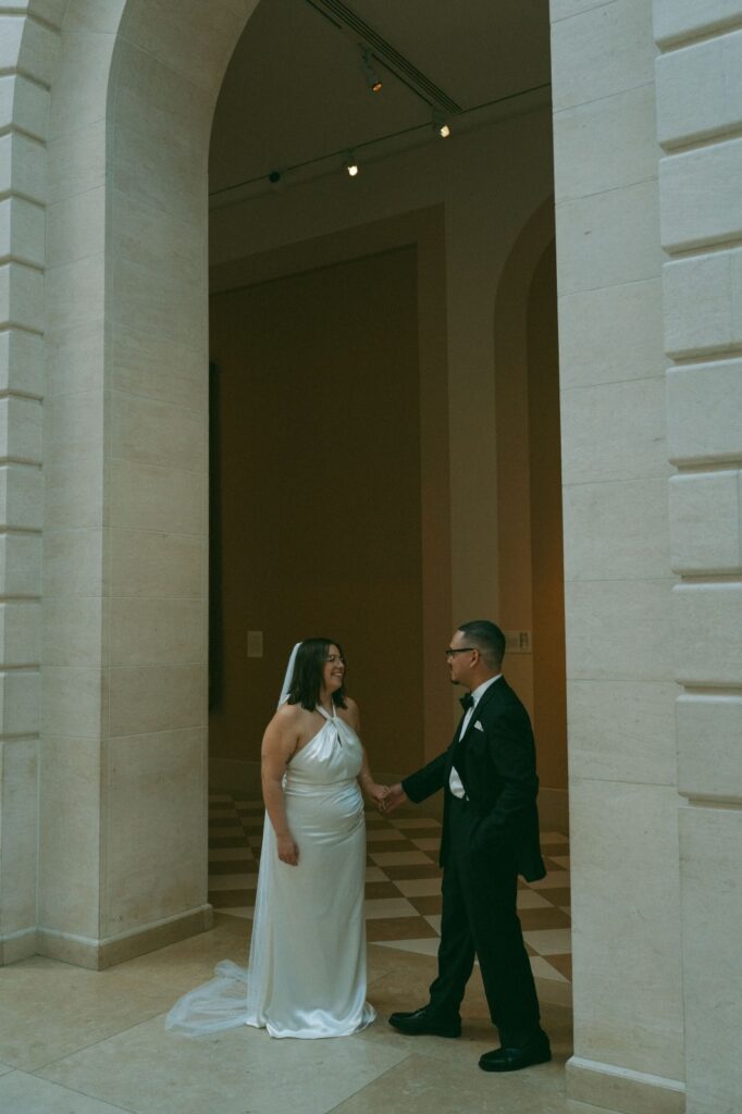 Bride and groom hold hands under a stone archway at NYPL elopement, shot by Elsie Goodman