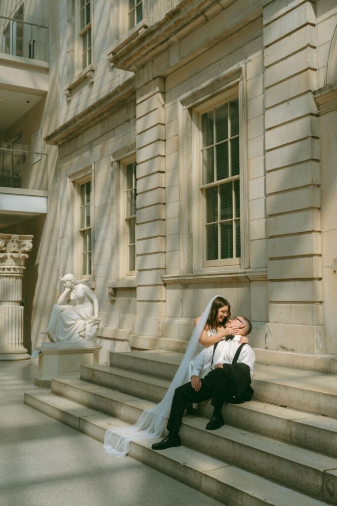Bride and groom sitting on steps and looking at each other in a sunspot at the MET after their elopement, by Elsie Goodman.