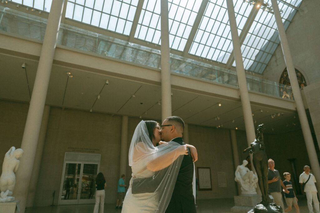 Bride and groom share a kiss under a skylight at a museum after eloping, shot by Elsie Goodman.