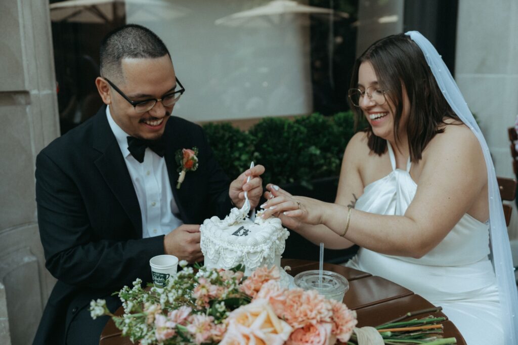 Bride and groom dig into wedding cake outside of Ralph's after their NYPL wedding ceremony, by Elsie Goodman