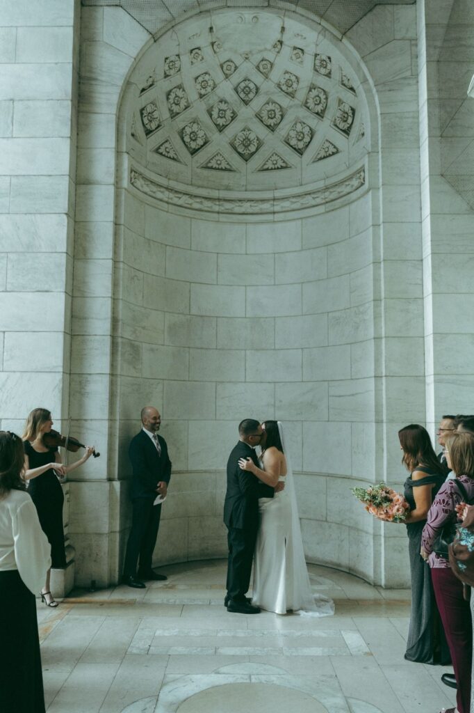 Bride and groom have a first kiss during their intimate NYPL wedding, shot by Elsie Goodman.