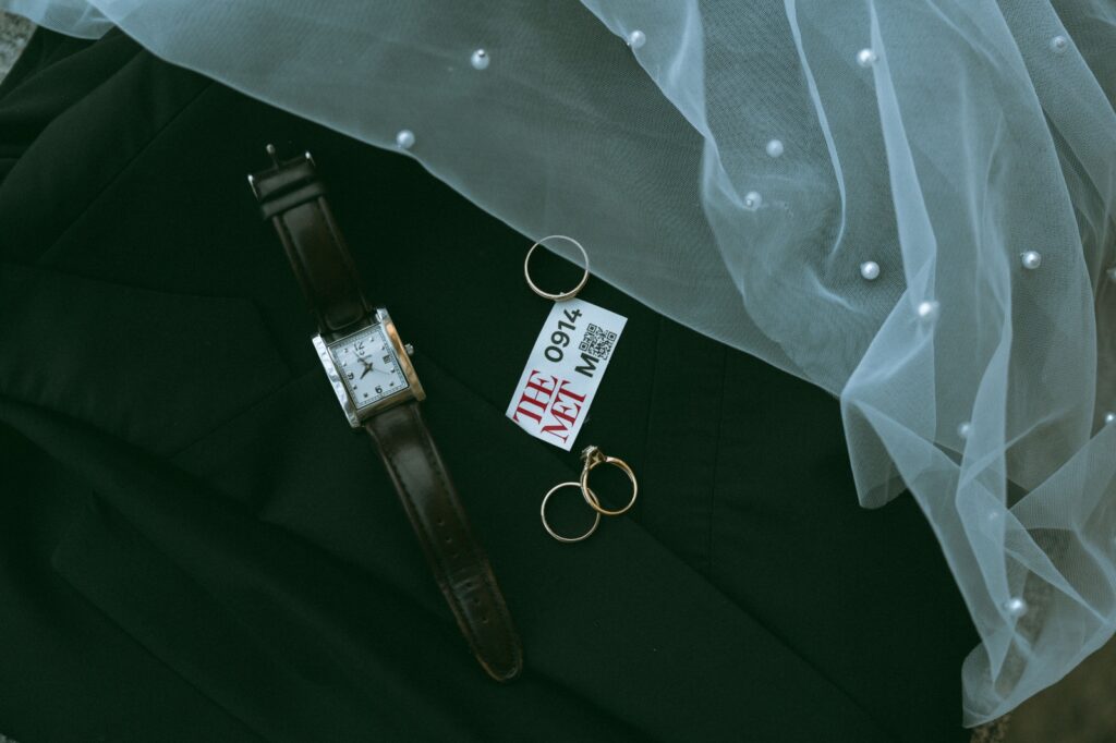 Details shot of watch, rings, and MET ticket on groom's jacket with bride's veil, by Elsie Goodman Photography.