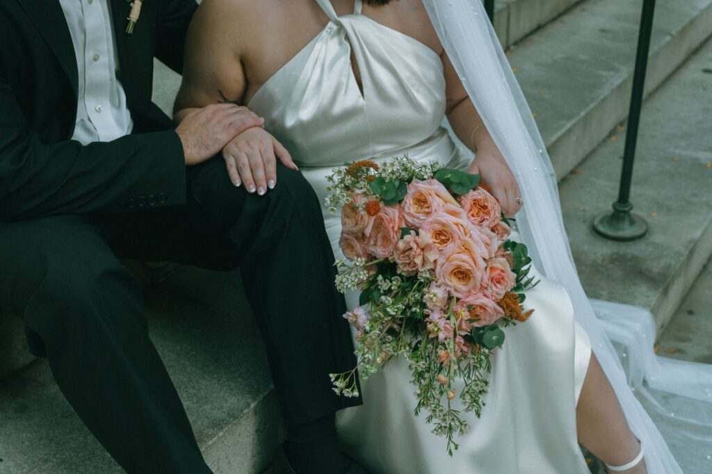 Close up of bride and groom sitting on NYPL steps, holding bouquet, by Elsie Goodman.