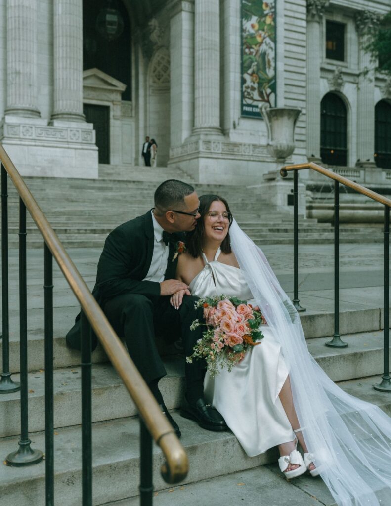 Bride and groom sit joyfully on the NYPL steps after eloping with big smiles, captured by Elsie Goodman.