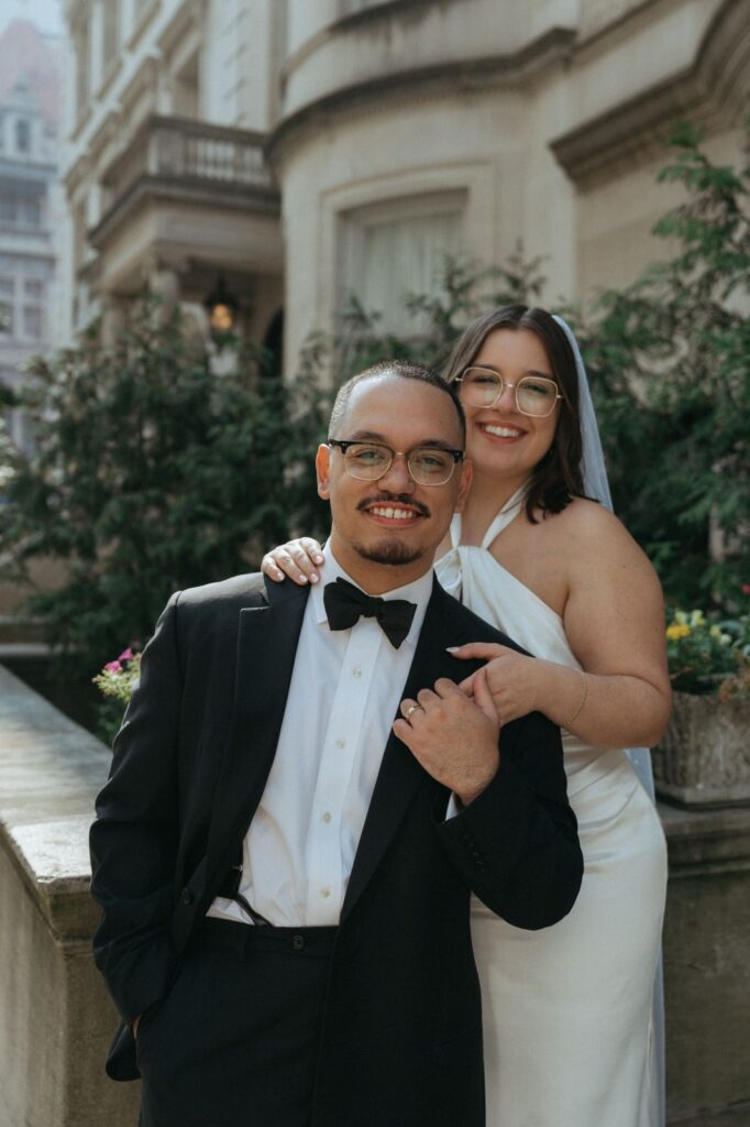 Bride stands behind groom with hand on his shoulder for NYC wedding portrait by Elsie Goodman.