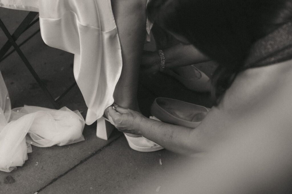 Woman helps bride buckle shoes before NYPL elopement, captured by Elsie Goodman Photography.