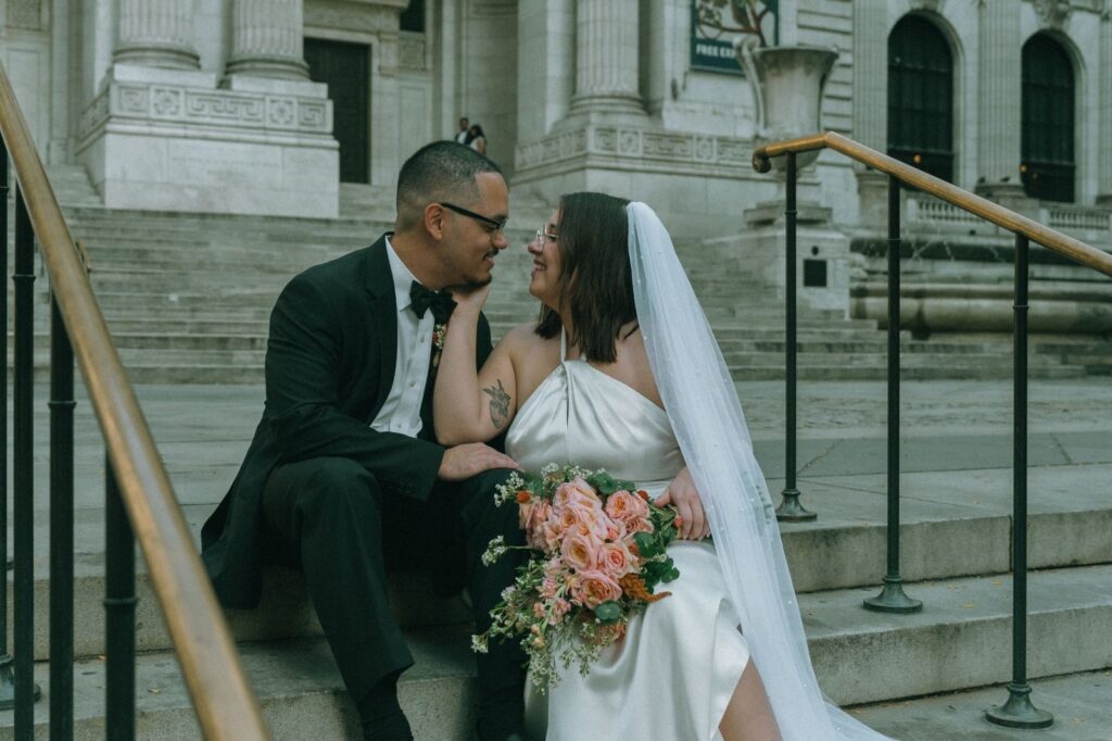 Bride and groom look at each other, sitting on steps of the NYPL after eloping, by Elsie Goodman.