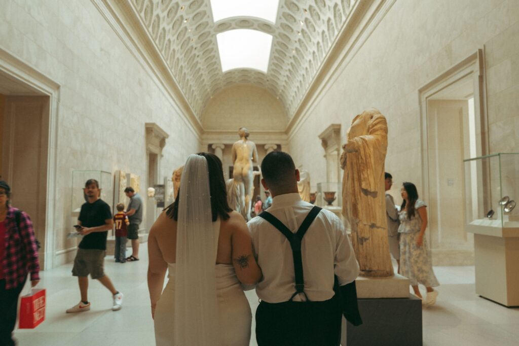 Back view of bride and groom walking through museum after eloping, by Elsie Goodman Photography.