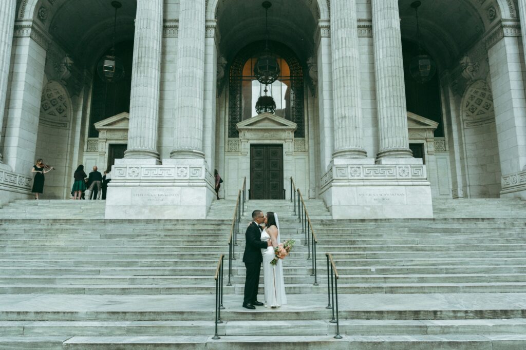 Bride and groom kiss on steps outside of New York Public Library after eloping, shot by Elsie Goodman.