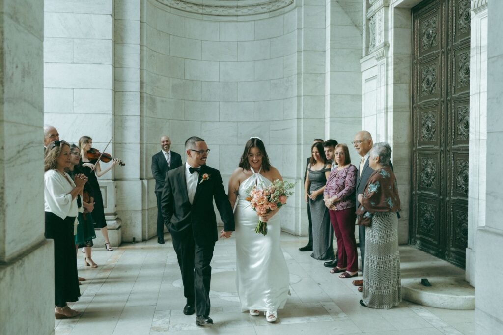 Bride and groom smiling, walking down the aisle after New York Public Library elopement, by Elsie Goodman.