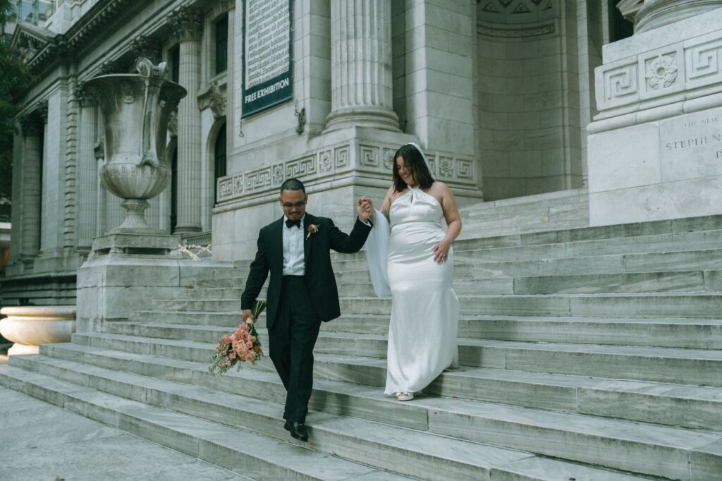 Bride and groom hold hands and walk down steps of NYPL after eloping, shot by Elsie Goodman Photography.