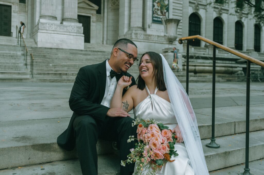 Bride and groom smile, sitting on steps of NYPL after their elopement, by Elsie Goodman.